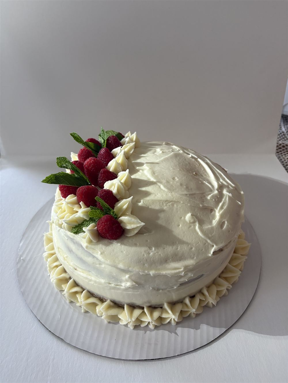 A frosted layer cake topped with raspberries and mint